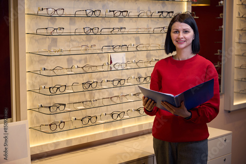 Brunette in red sweatshirt stands at display case with glasses photo