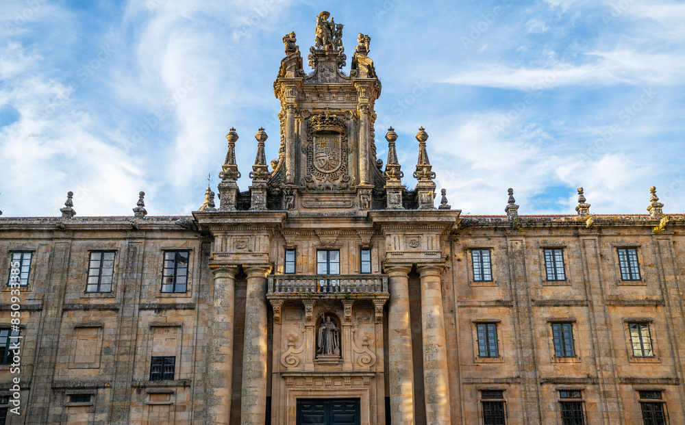 Obraz premium Baroque facade of a historical building with ornate sculptures and emblem, set against a blue sky with wispy clouds, possibly in Europe during spring