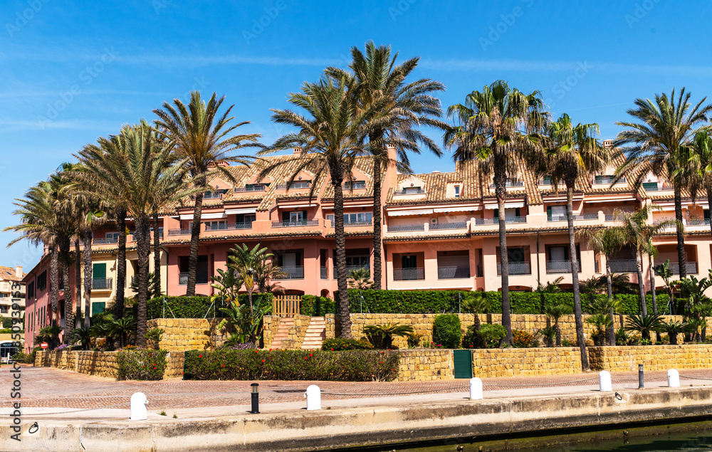 Luxurious Mediterranean terracotta-roofed apartments flanked by palm trees, showcasing coastal Spanish architecture in a serene residential area. Luxurious Mediterranean terracotta-roofed apartments flanked by palm trees, showcasing coastal Spanish architecture in a serene residential area.