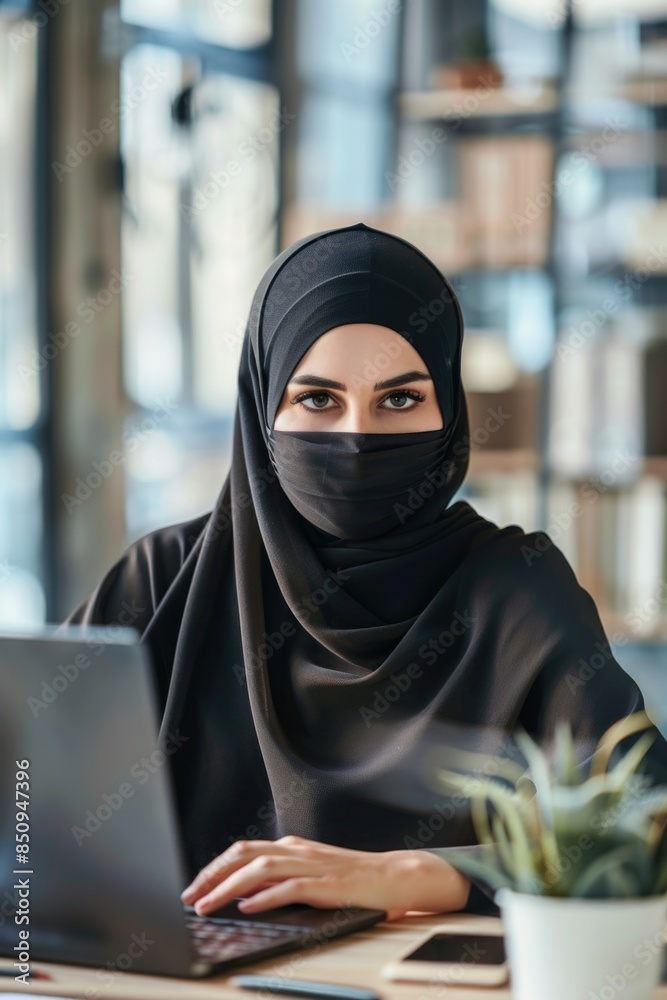 A Muslim woman working on her laptop while wearing a traditional black hijab, great for education or workplace concepts A Muslim woman working on her laptop while wearing a traditional black hijab, great for education or workplace concepts