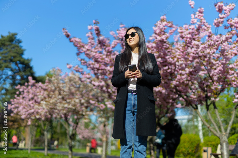 A young Japanese woman, styled fashionably, enjoys the springtime sakura blossoms in a picturesque park. A young Japanese woman, styled fashionably, enjoys the springtime sakura blossoms in a picturesque park.