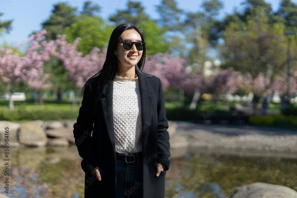 An elegant Asian woman smiles while posing in an urban park, exuding modern style and charm. An elegant Asian woman smiles while posing in an urban park, exuding modern style and charm.