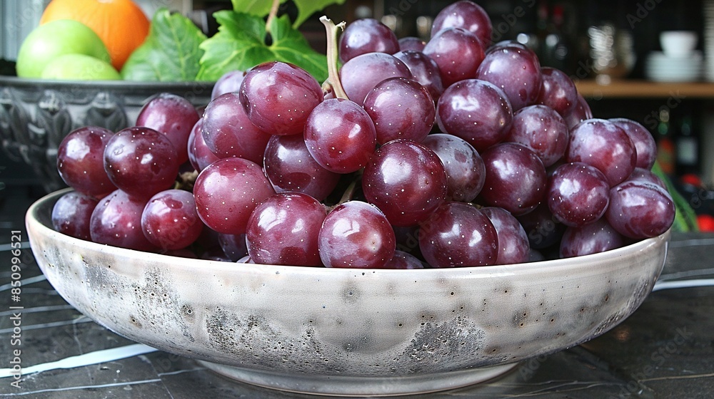 A bowl of grapes sits beside orange and grape bowls on a table A bowl of grapes sits beside orange and grape bowls on a table