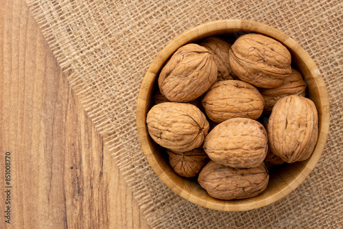Overhead view of a wooden bowl full of shelled walnuts on a piece of burlap