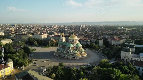 Aerial drone view of St. Alexander Nevsky Cathedral in the Sofia city, Bulgaria. Footage of the iconic Bulgarian orthodox church during sunrise surrounded by green trees. 