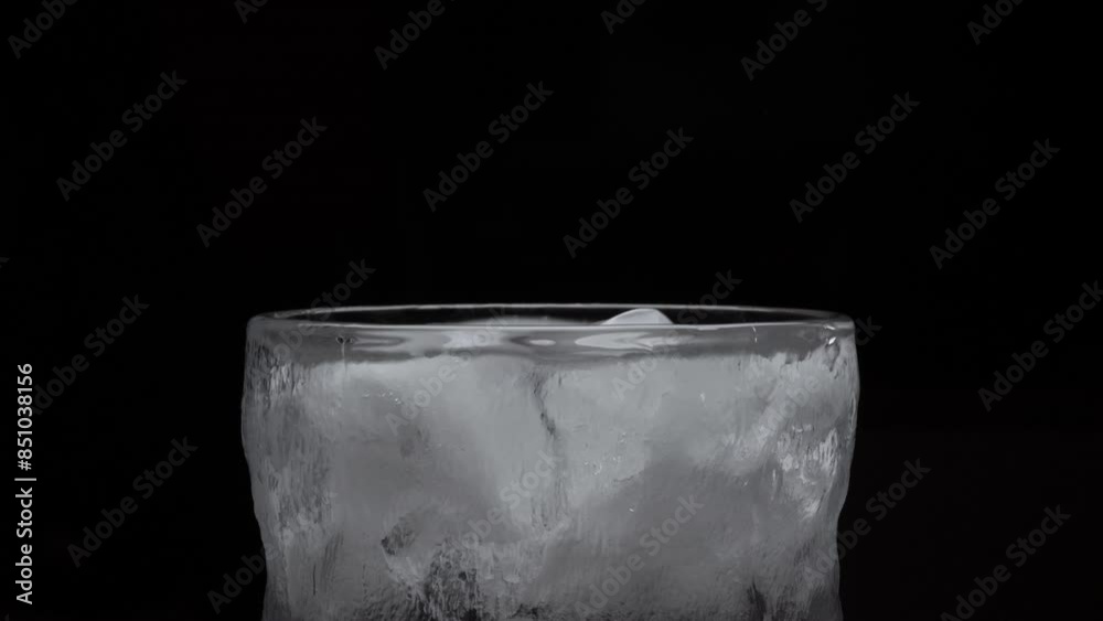 Close up of ice cubes falling into an glass on a dark background