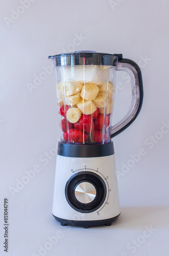 White mixer with fruits and berries, banana, strawberry on gray background, making smoothie, vertical photo photo