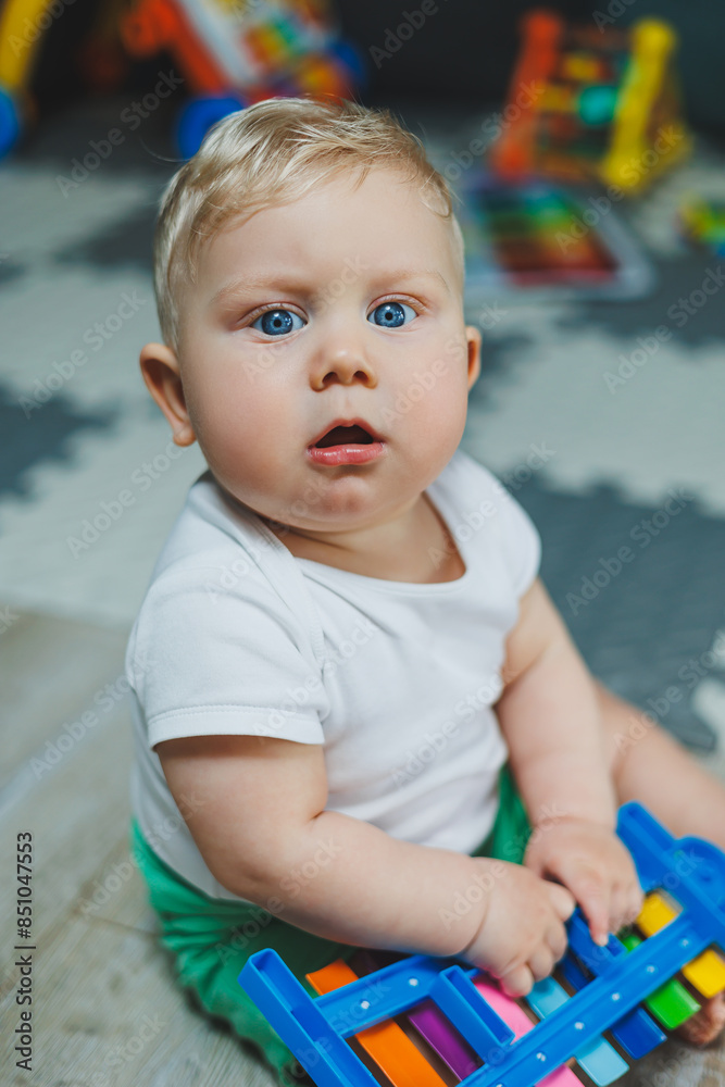 A fair-haired boy of 10 months sits on the floor at home and plays with toys. Educational toys for babies. Self-development of the child. A fair-haired boy of 10 months sits on the floor at home and plays with toys. Educational toys for babies. Self-development of the child.