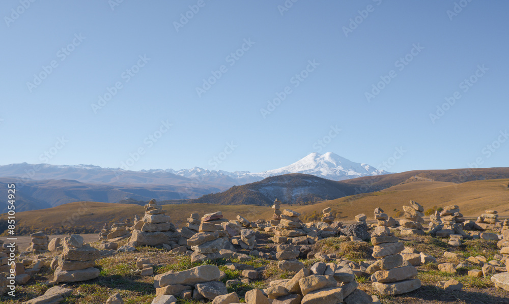 Mountain Elbrus. Autumn Elbrus. Autumn in the Caucasus mountains. Gilli-Suu district. Landscape of snow-capped mountains through stone pyramids. Snowy peaks. Panorama of Elbrus.