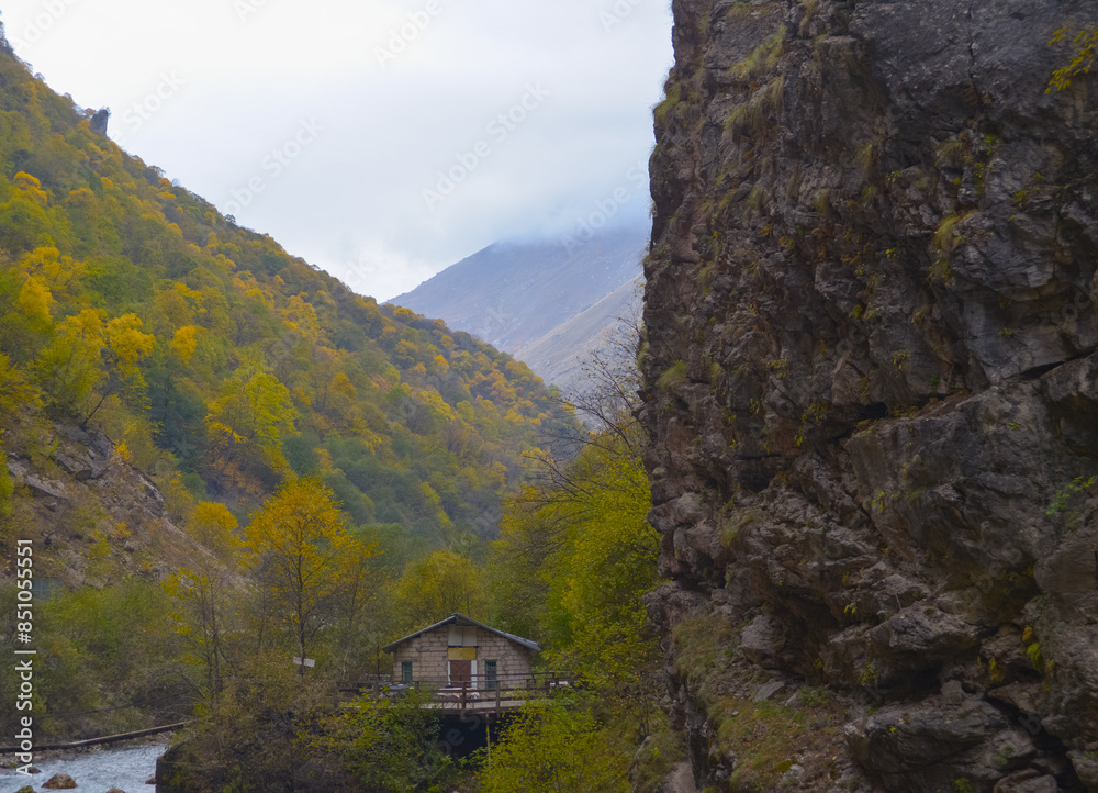 A small house near a mountain river and the foot of the misty mountains. North Caucasus, Russia.