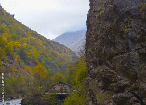 Obraz na płótnie A small house near a mountain river and the foot of the misty mountains. North Caucasus, Russia. w salonie