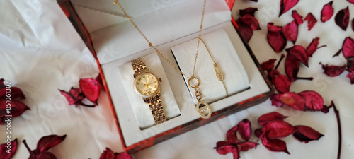 Gold wristwatch necklace and bracelet set in open gift box surrounded by red potpourri