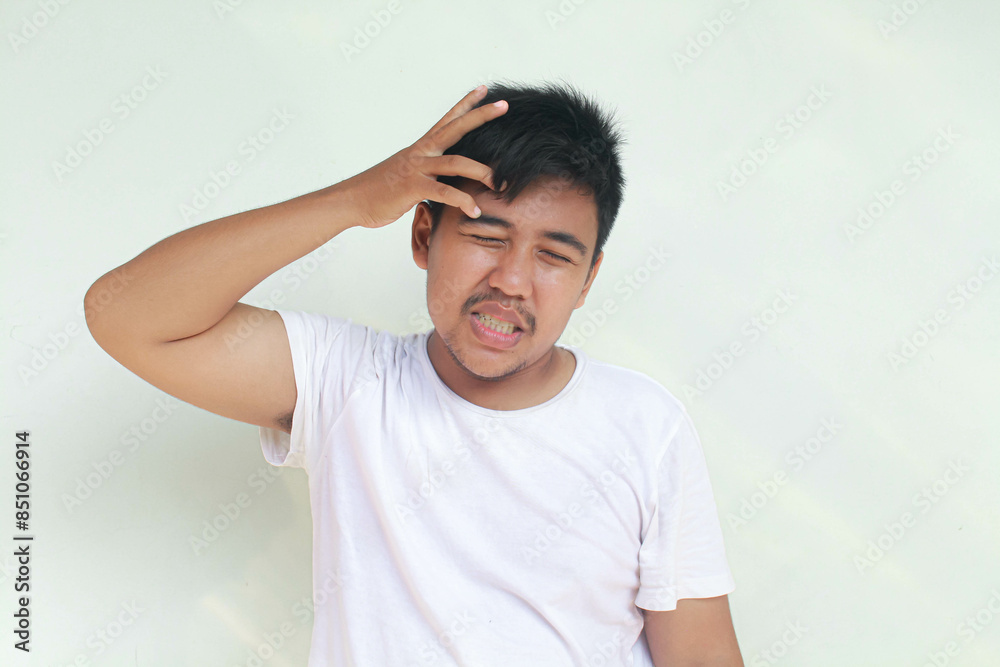 A portrait of an Asian man wearing a white shirt isolated by gray background looks depressed. A portrait of an Asian man wearing a white shirt isolated by gray background looks depressed.