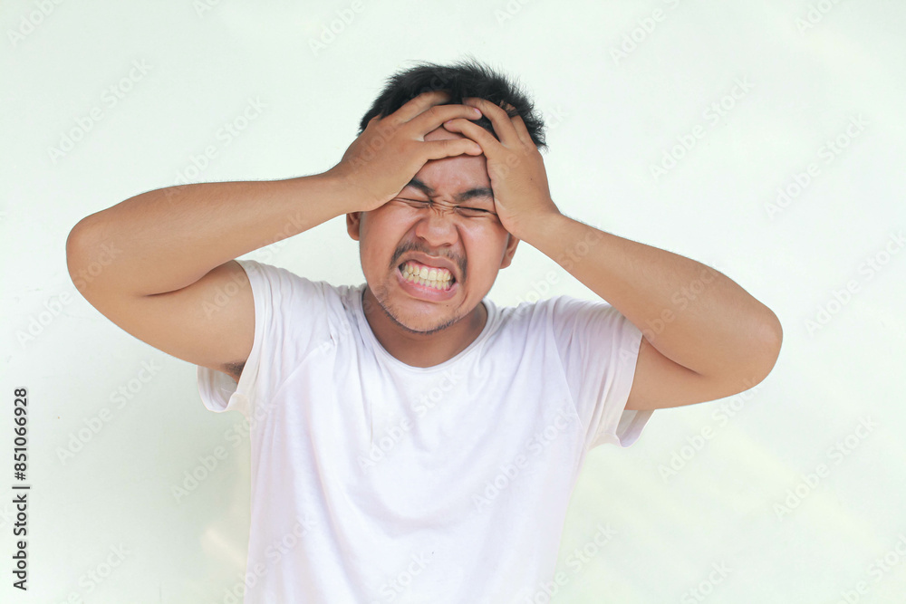 A portrait of an Asian man wearing a white shirt isolated by gray background looks depressed. A portrait of an Asian man wearing a white shirt isolated by gray background looks depressed.