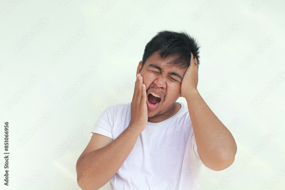 Toothache and headache young Asian man with hurt emotion wear white shirt. Isolated in gray background. Toothache and headache young Asian man with hurt emotion wear white shirt. Isolated in gray background.