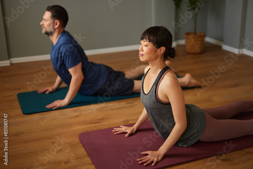 Caucasian man and Asian woman practicing yoga together in yoga studio