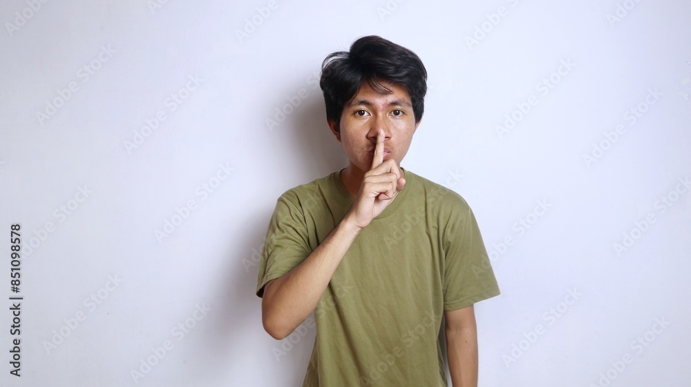 Young Asian man gestures with his hand to cover his mouth as if telling him to be quiet Young Asian man gestures with his hand to cover his mouth as if telling him to be quiet