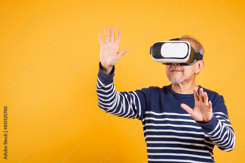 Portrait Asian smiling old man touching at something in a virtual reality glasses headset studio shot isolated yellow background, Excited happy senior man pensioner using VR play simulation game Portrait Asian smiling old man touching at something in a virtual reality glasses headset studio shot isolated yellow background, Excited happy senior man pensioner using VR play simulation game