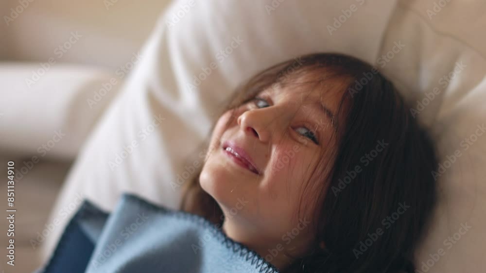 A young boy lies on a bed, his face partially covered by a blue blanket, smiling brightly at the camera. A young boy lies on a bed, his face partially covered by a blue blanket, smiling brightly at the camera.