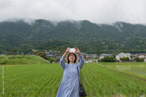 里山の田園風景をスマートフォンで撮影する女性 photo