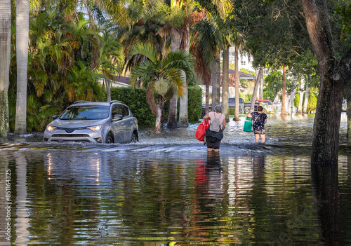Wallpaper Mural After the 2024 Hallandale Beach flood, residents wade through floodwaters carrying bags, while a car navigates the submerged street. The scene highlights the community's resilience and recovery effort Torontodigital.ca