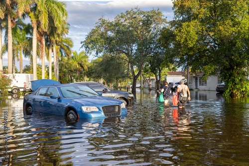 Wallpaper Mural After the 2024 Hallandale Beach flood, residents wade through floodwaters carrying bags, while a car navigates the submerged street. The scene highlights the community's resilience and recovery effort Torontodigital.ca