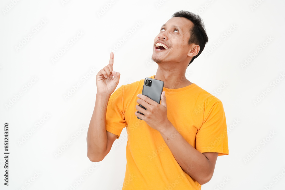 a young man wearing a yellow t-shirt points his finger up holding a cell phone. With a plain white background a young man wearing a yellow t-shirt points his finger up holding a cell phone. With a plain white background
