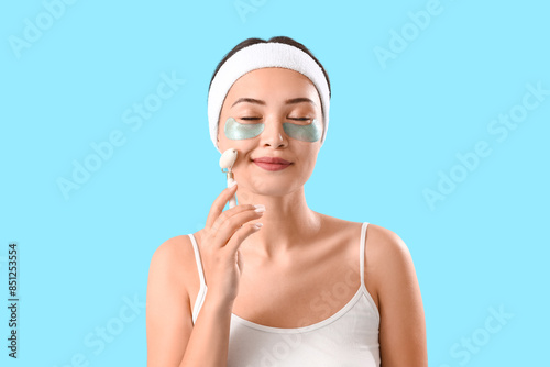Wallpaper Mural Pretty young woman with under-eye patches and facial massage roller on blue background Torontodigital.ca