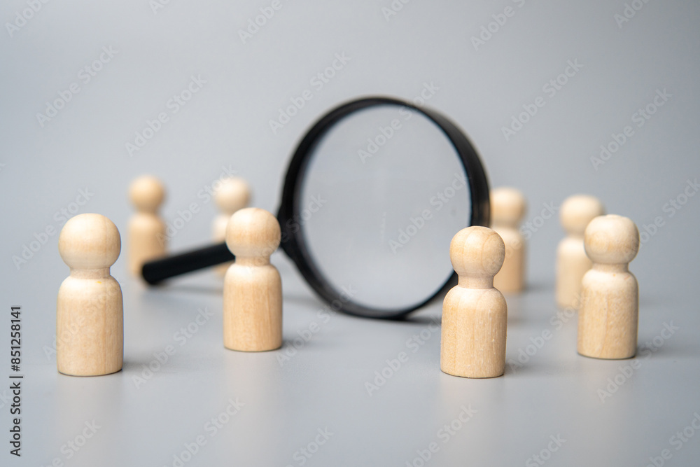 Obraz premium Wooden dolls and magnifying glass. Talent acquisition, recruitment and hiring concept.