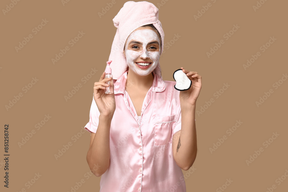 Young woman with reusable cotton pad and cleanser on brown background