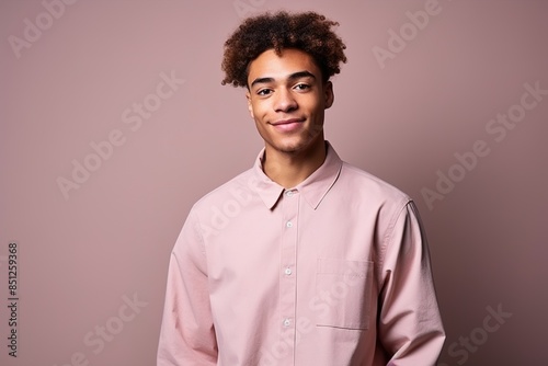 A young man with a black afro is wearing a pink shirt and smiling