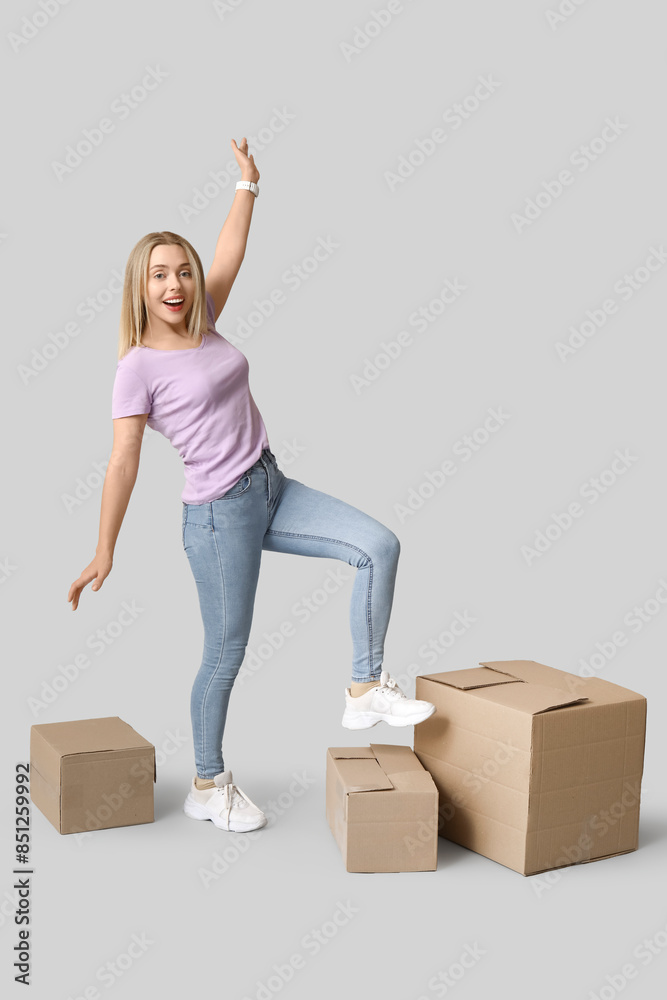 Happy young woman with cardboard boxes on grey background. Moving into new house concept