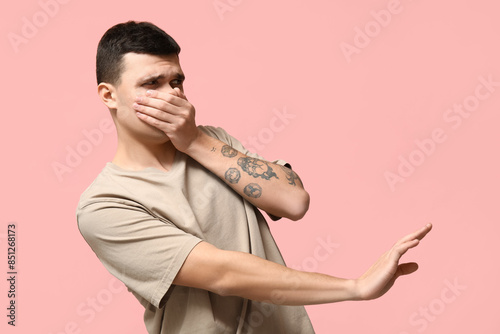 Handsome young man feeling bad smell on pink background photo