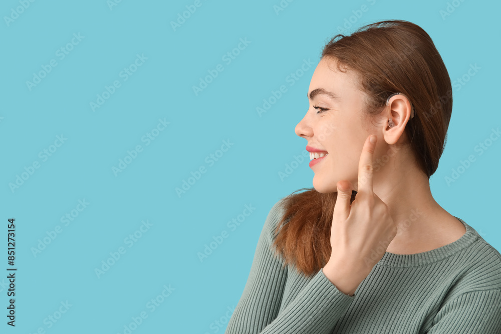 Happy young woman pointing at hearing aid on blue background Happy young woman pointing at hearing aid on blue background