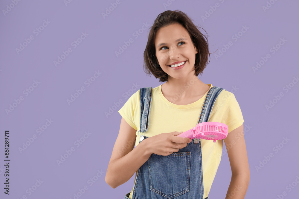 Young woman with pink portable electric fan on lilac background Young woman with pink portable electric fan on lilac background