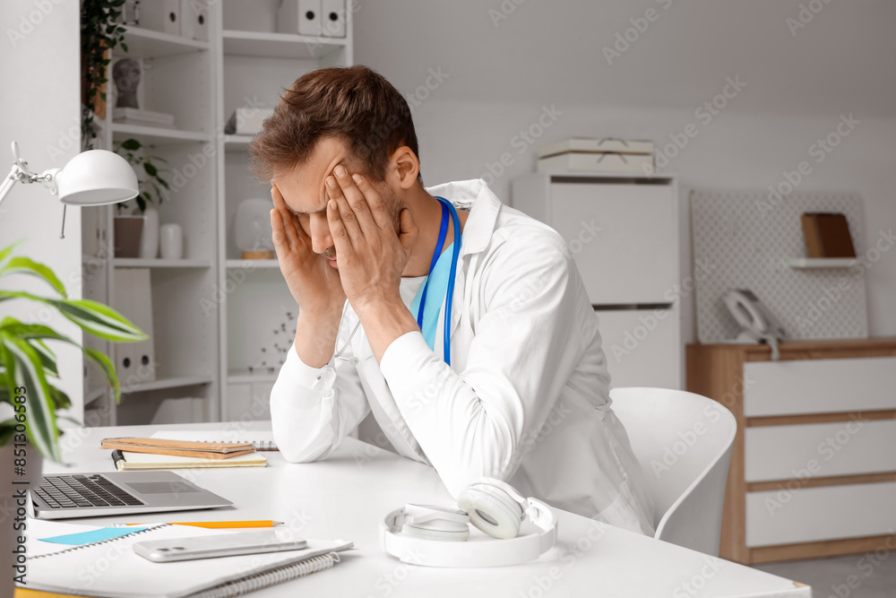 Tired medical intern sitting at table in clinic