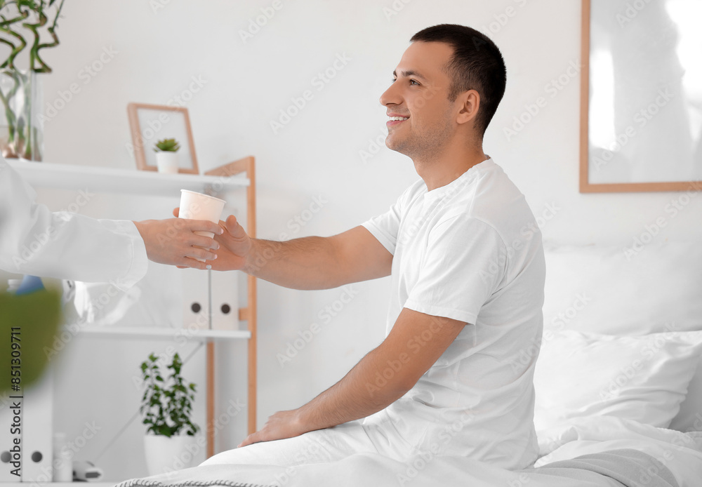 Male patient taking cup of water from doctor in hospital ward
