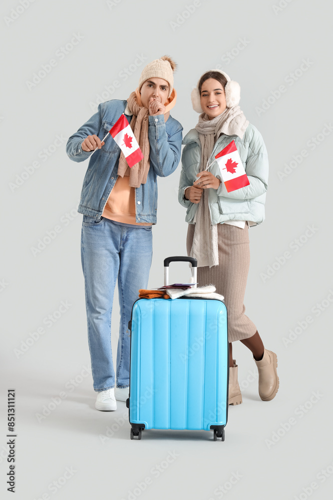 Young couple of tourists in warm clothes with flags of Canada on light background Young couple of tourists in warm clothes with flags of Canada on light background