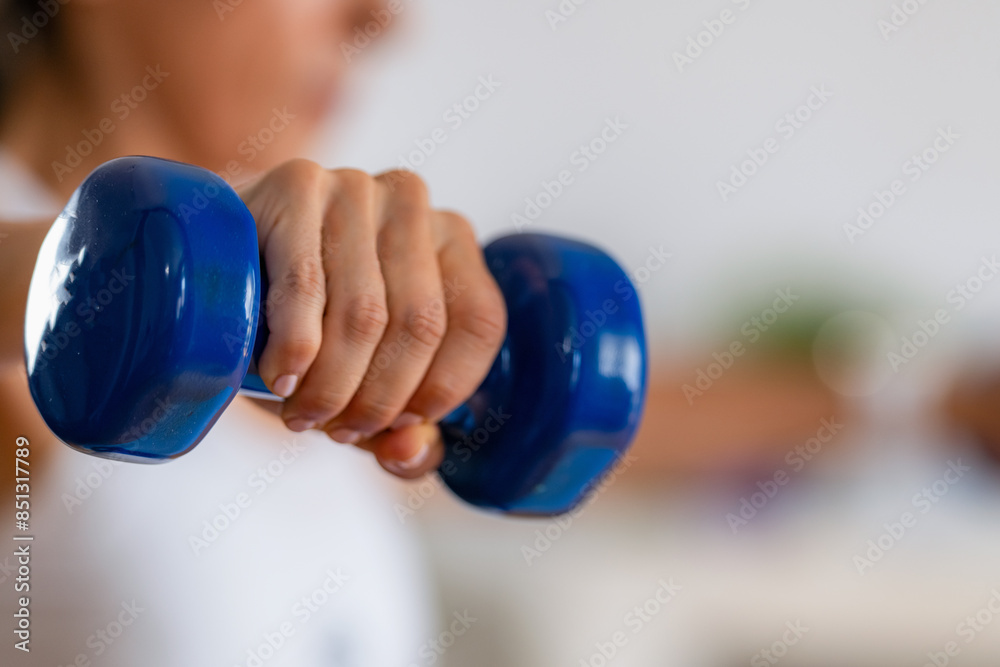 A woman exercises at home, focusing on her hand holding dumbbells, showcasing the determination of home fitness routines A woman exercises at home, focusing on her hand holding dumbbells, showcasing the determination of home fitness routines