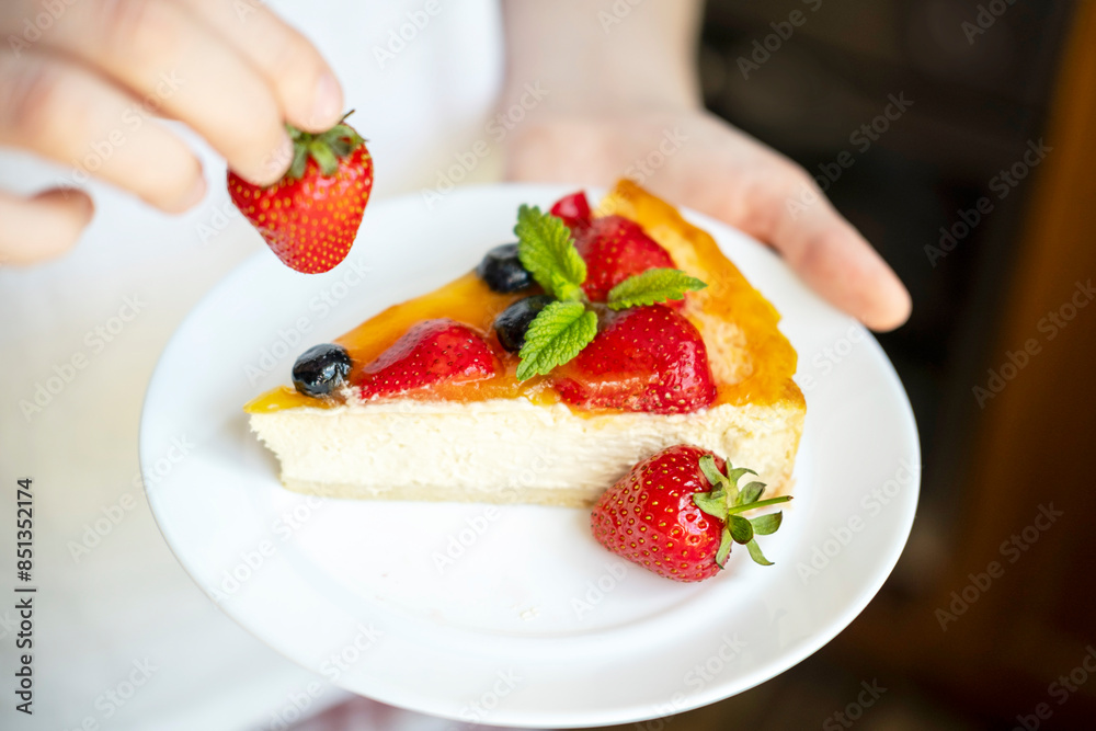 Man holding a plate with appetizing and delicious cheesecake cooked at home. In his hand is a strawberry. The concept of cooking tasty and healthy food. Man holding a plate with appetizing and delicious cheesecake cooked at home. In his hand is a strawberry. The concept of cooking tasty and healthy food.