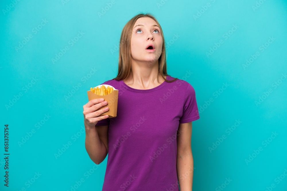 Young Russian woman catching french fries isolated on blue background looking up and with surprised expression Young Russian woman catching french fries isolated on blue background looking up and with surprised expression
