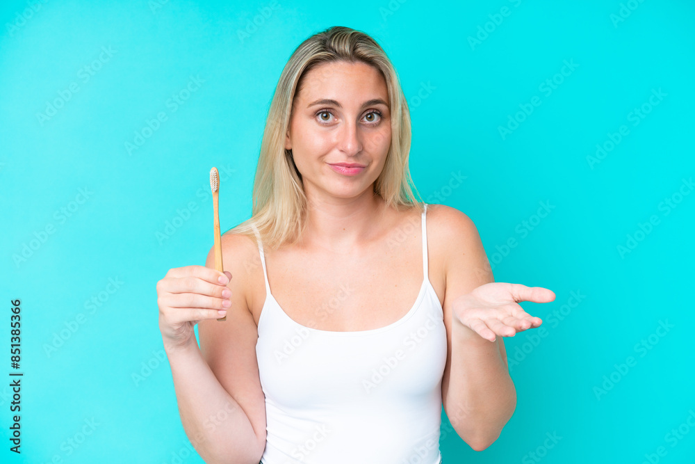 Young caucasian woman brushing teeth isolated on blue background making doubts gesture while lifting the shoulders Young caucasian woman brushing teeth isolated on blue background making doubts gesture while lifting the shoulders