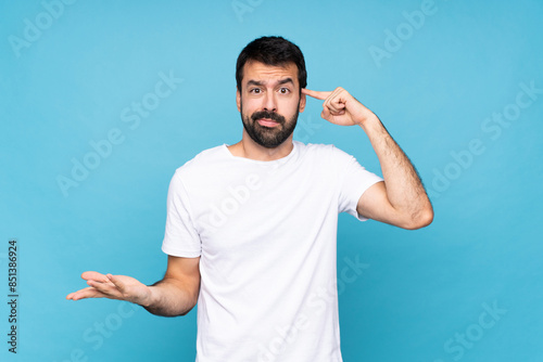 Young man with beard over isolated blue background making the gesture of madness putting finger on the head