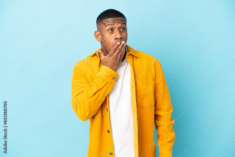 Obraz premium Young latin man isolated on blue background yawning and covering wide open mouth with hand