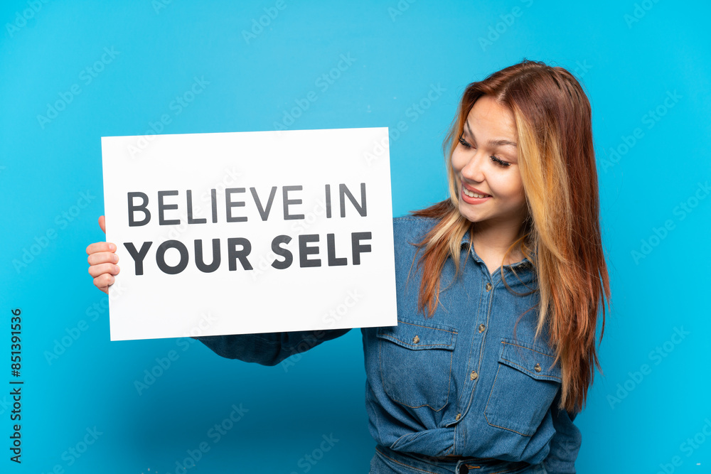 Teenager girl over isolated blue background holding a placard with text Believe In Your Self Teenager girl over isolated blue background holding a placard with text Believe In Your Self