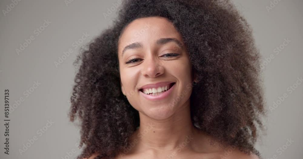 Beauty and Healthcare - Beautiful African American woman with curly afro hairstyle and clear, healthy skin, posing and looking at camera with toothy smile while standing against gray studio background Beauty and Healthcare - Beautiful African American woman with curly afro hairstyle and clear, healthy skin, posing and looking at camera with toothy smile while standing against gray studio background