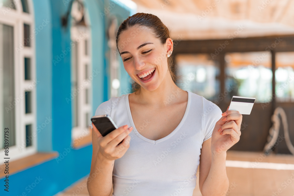 Young pretty woman at outdoors buying with the mobile with a credit card Young pretty woman at outdoors buying with the mobile with a credit card
