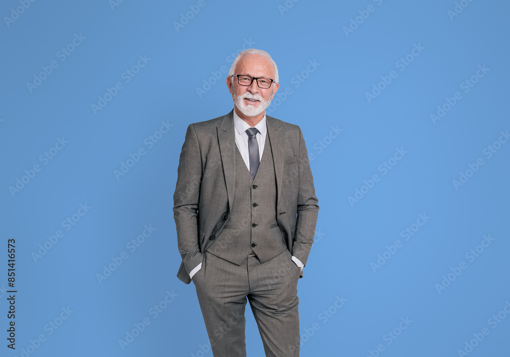 Portrait of confident senior businessman with hands in pockets standing on isolated blue background Portrait of confident senior businessman with hands in pockets standing on isolated blue background