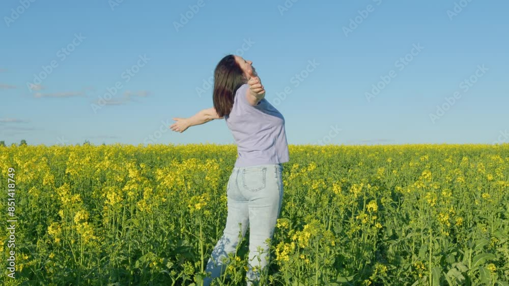 Woman Standing In Yellow Rapeseed Field Raising Her Arms Expressing Freedom. Beautiful Healthy Caucasian White Woman Standing In Blooming Rapeseed Field And Looking At Horizon. Woman Standing In Yellow Rapeseed Field Raising Her Arms Expressing Freedom. Beautiful Healthy Caucasian White Woman Standing In Blooming Rapeseed Field And Looking At Horizon.