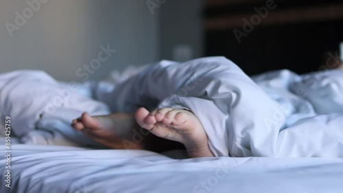 The view of a small child's feet sticking out from under a large and fluffy blanket lying on a large snow-white bed illustrates the concept of sleep and peace.